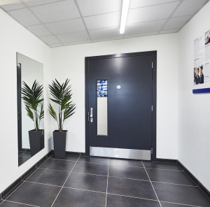 Black security door with glass panel and a keypad lock in a white room with black floor